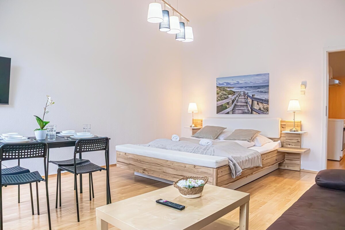 A bedroom with a wooden bed, bedside tables with lamps, a dining area with chairs and a table, and a painting on the wall.