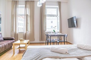 Ein Hotelzimmer mit Bett, Sofa, Tisch mit Stühlen, einem an der Wand befestigten Fernseher und einem Fenster mit Vorhängen.