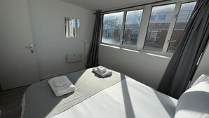 Une chambre d’hôtel avec un lit, une fenêtre, une porte et un thermostat fixé au mur.
