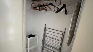 Un petit placard blanc, équipé d’un étendoir métallique et d’une étagère sur laquelle se trouve un objet noir.