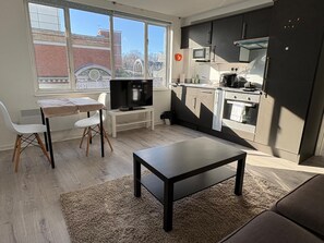 A compact living space with a kitchenette, a dining area with a table and chairs, and a television. - The Elden - No.18 (London)