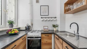 A compact kitchen with a gas stove, oven, and sink, wooden cabinets, and a black countertop. - Lumina cozy 3-room apartment in Warsaw (Warszawa BIG)