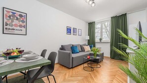 A modern living room with a grey sofa, a dining table set for two, and a green rug. - Lumina cozy 3-room apartment in Warsaw (Warszawa BIG)