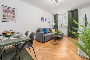 Una sala moderna con un sofá gris, una mesa de comedor para dos personas y una alfombra verde.