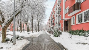 A snow-covered pathway flanked by trees and red apartment buildings. - Lumina cozy 3-room apartment in Warsaw (Warszawa BIG)