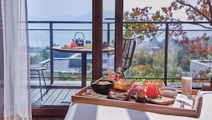Ein Esstisch mit verschiedenen Speisen und einem Getränk auf einem Balkon mit Blick auf eine Stadtansicht und Bäume.