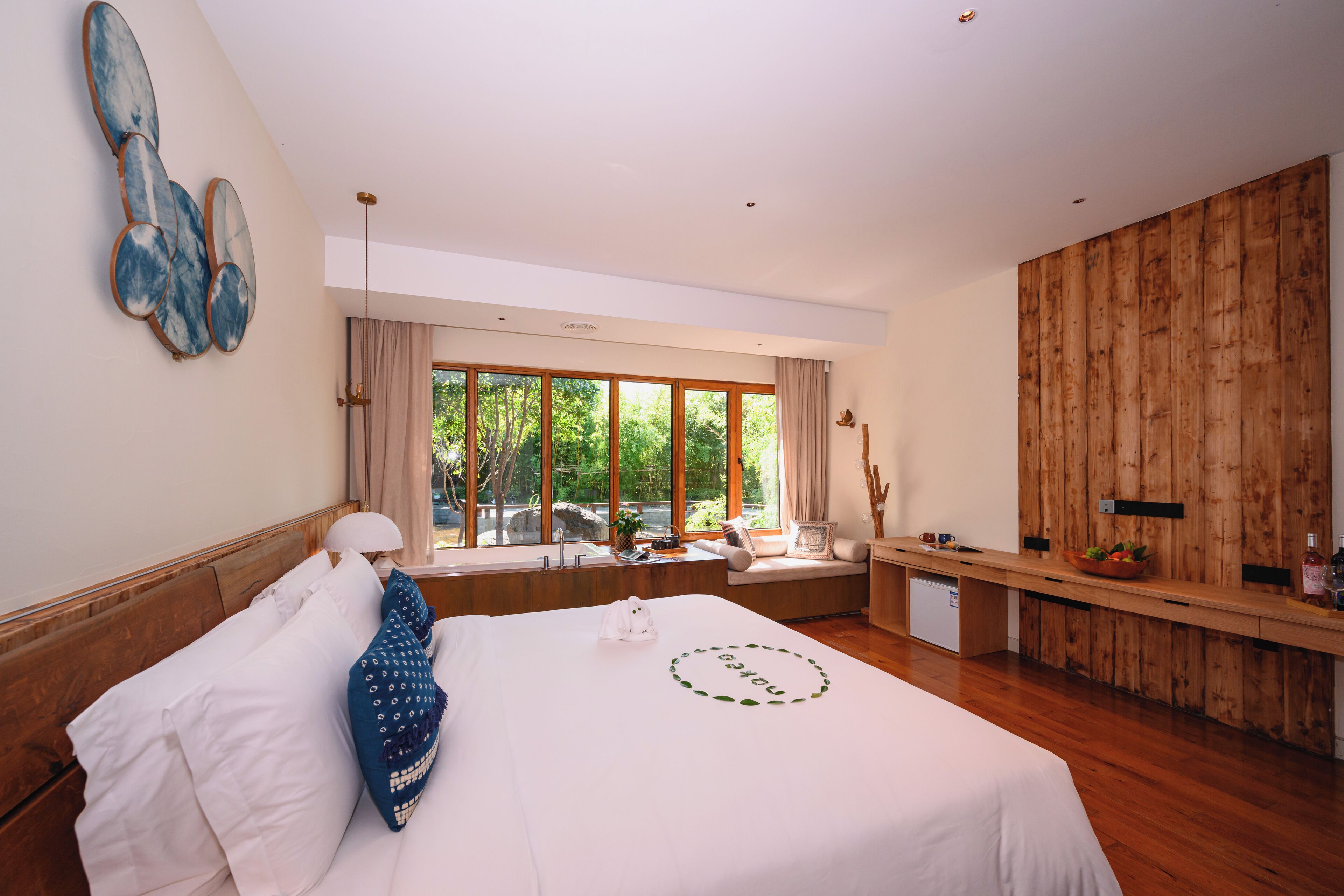 A modern hotel room with a large bed, a wooden desk, and a view of the outdoors.