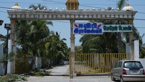 A gated entrance with a sign in a foreign script, palm trees, and a car parked in front. - Hotel Zen zones  (Chennai)