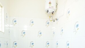 A bathroom with a toilet, blue tiles, a shower, and a water heater on the wall. - Hotel Zen zones  (Chennai)