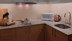 Een kleine keuken met grijze kastjes, een magnetron, een waterkoker en een spoelbak.
