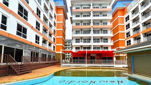 A swimming pool with a red canopy and a building with orange and white exterior walls. - Modern 1-bedroom Condo With Pool View - Nordic Trend 4, Pratumnak Hill (Pattaya)