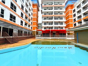 Ein Swimmingpool mit rotem Sonnensegel und ein Gebäude mit orangefarbenen und weißen Außenwänden.
