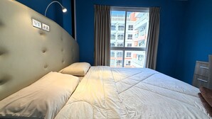 A bedroom with a large bed, a headboard, a window with curtains, and a view of buildings outside. - Modern 1-bedroom Condo With Pool View - Nordic Trend 4, Pratumnak Hill (Pattaya)