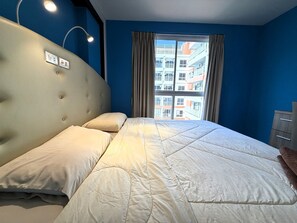 Ein Schlafzimmer mit einem großen Bett, einem Kopfteil, einem Fenster mit Vorhängen und Blick auf Gebäude.