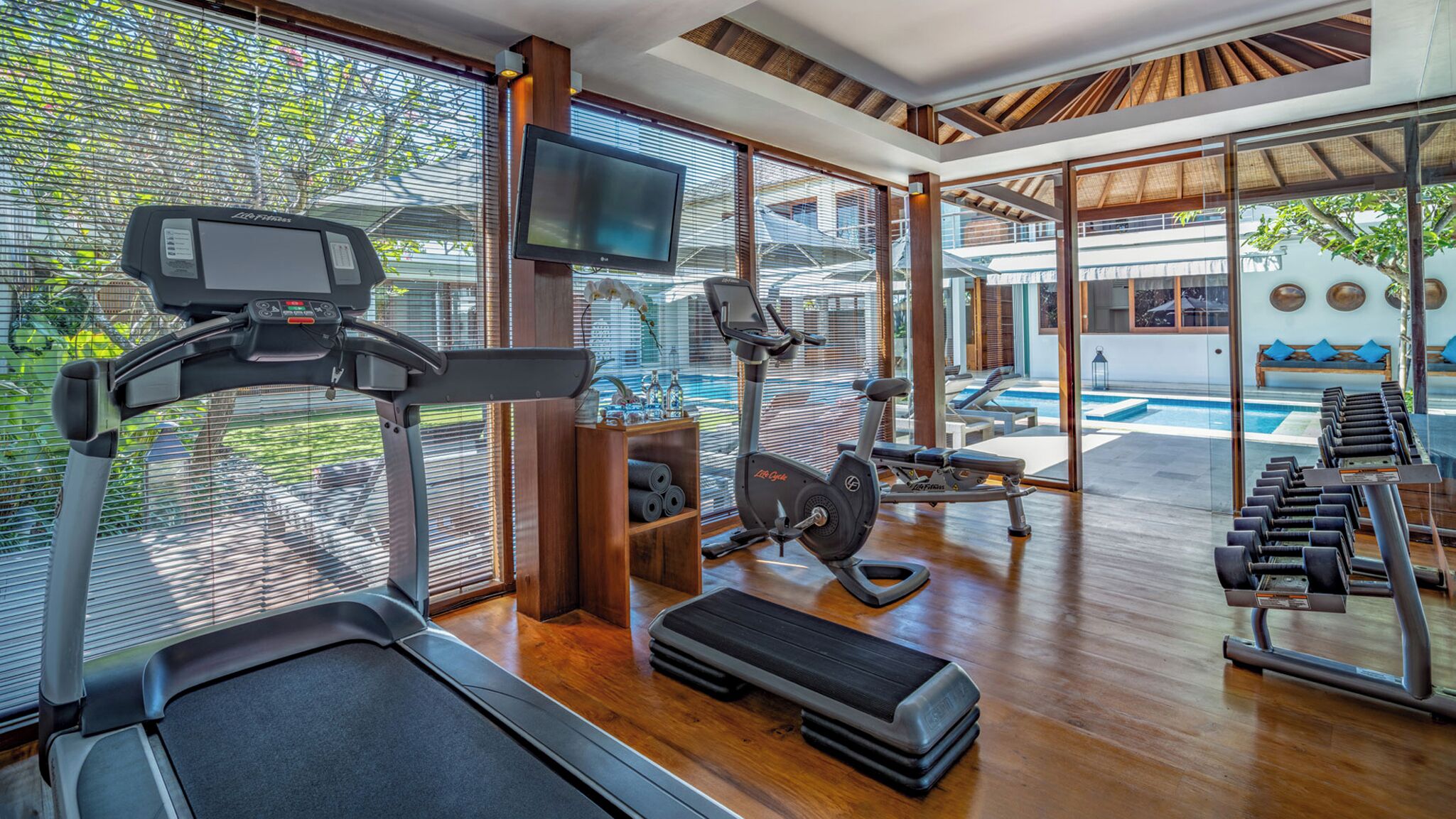 A modern gym with cardio equipment, weights, and a TV.
