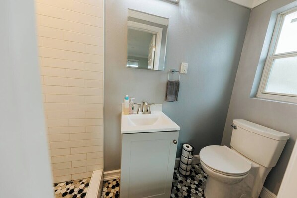 Ein Badezimmer mit Toilette, Waschbecken und Spiegel. Ein Handtuch hängt an der Wand und ein Mülleimer steht neben der Toilette.