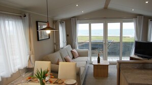Un salon avec un canapé, une table à manger dressée pour deux personnes, un téléviseur et une grande fenêtre donnant sur la mer.