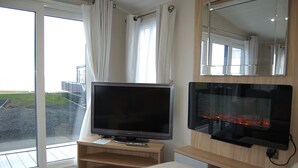 Un salon moderne avec un téléviseur à écran plat posé sur un meuble en bois, une cheminée en verre et une grande fenêtre agrémentée de rideaux.