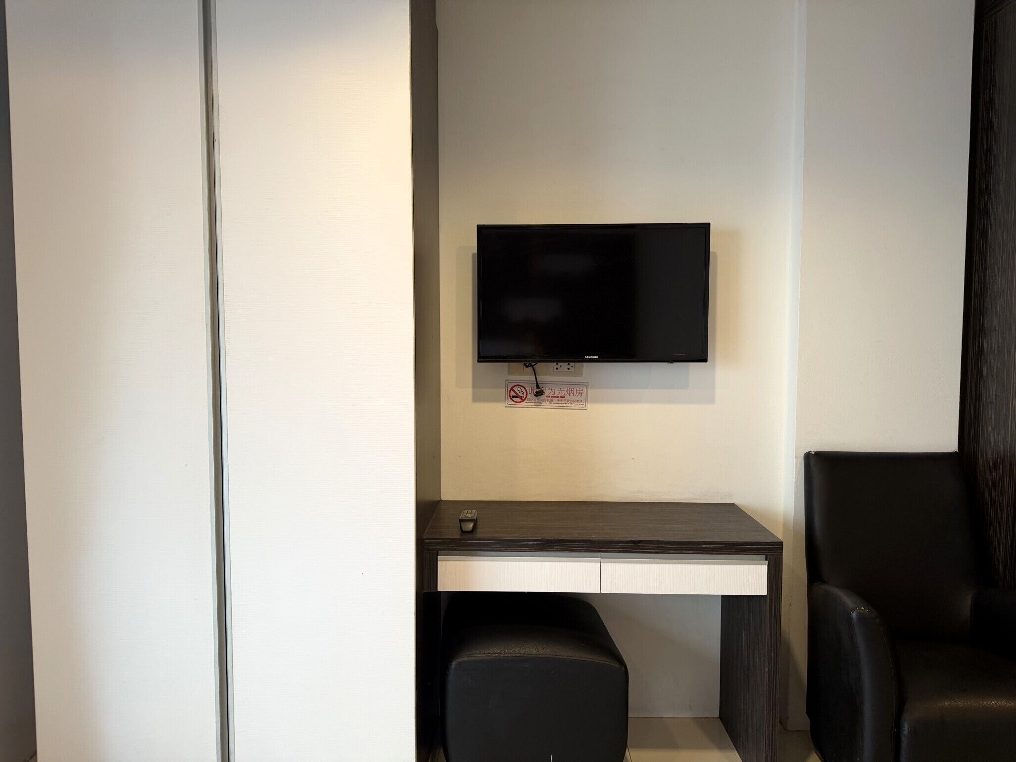 A modern room with a flat-screen TV mounted on the wall, a desk with a chair, and a bench.