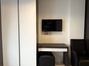 Ein modernes Zimmer mit einem flachbildfernseher an der Wand, einem Schreibtisch mit Stuhl und einer Sitzbank.