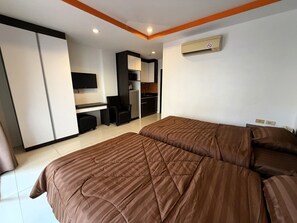 Ein Hotelzimmer mit zwei Betten, einem Schreibtisch, einem Sessel, einem Fernseher und einer Küchenzeile.