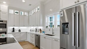 A modern kitchen with white cabinetry, stainless steel appliances, and a built-in dishwasher. - Brand-New Oceanfront Showstopper | 6 En-Suite Bedrooms, Pool, 2 Hot Tubs, Elevator (North Myrtle Beach)