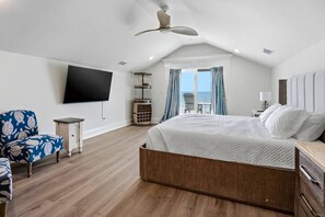 A bedroom with a large bed, a flat-screen TV, a ceiling fan, and a view of the ocean through the window. - Brand-New Oceanfront Showstopper | 6 En-Suite Bedrooms, Pool, 2 Hot Tubs, Elevator (North Myrtle Beach)