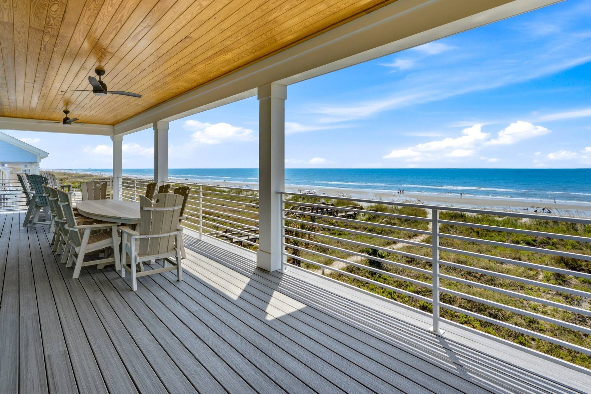 A wooden deck with a table and chairs, overlooking a beach with a railing.