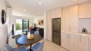 A modern kitchen with light wood cabinets, a stainless steel refrigerator, and a dining area with a round table and chairs.