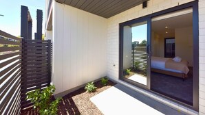 A modern hotel room with a sliding glass door, a bed, and a small balcony with a metal fence.