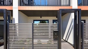 A gated entrance with a modern design, a mailbox, and a building with a balcony in the background.