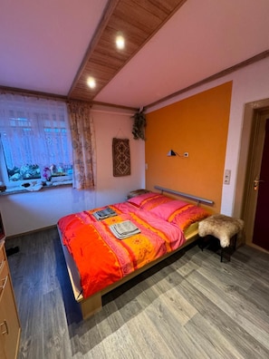 Een slaapkamer met een bed, een raam met gordijnen, een wandlamp en een deur.