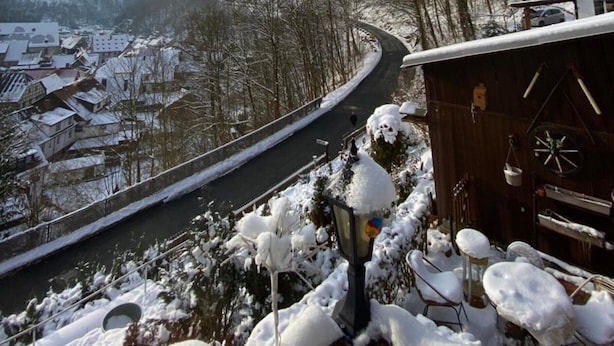 Ett snötäckt landskap med en slingrande väg, en träbyggnad med uteservering och en vy över en stad i bakgrunden.