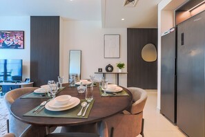A modern dining area with a round table set for two, a flat-screen TV, and a refrigerator. - Burj Crown Residences - Downtown Dubai (Dubai)