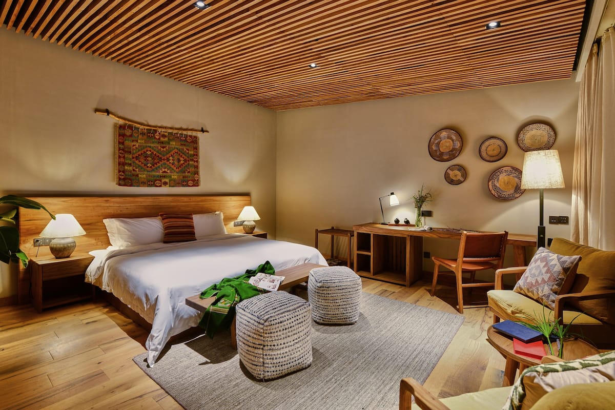 Un dormitorio bien iluminado con techo de madera, una cama grande, un escritorio y una zona de estar.