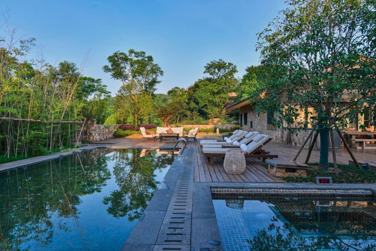 Un área de piscina tranquila al aire libre con sillas de descanso, una terraza de madera y un muro de piedra.