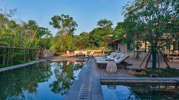 A serene outdoor pool area with lounge chairs, a wooden deck, and a stone wall.