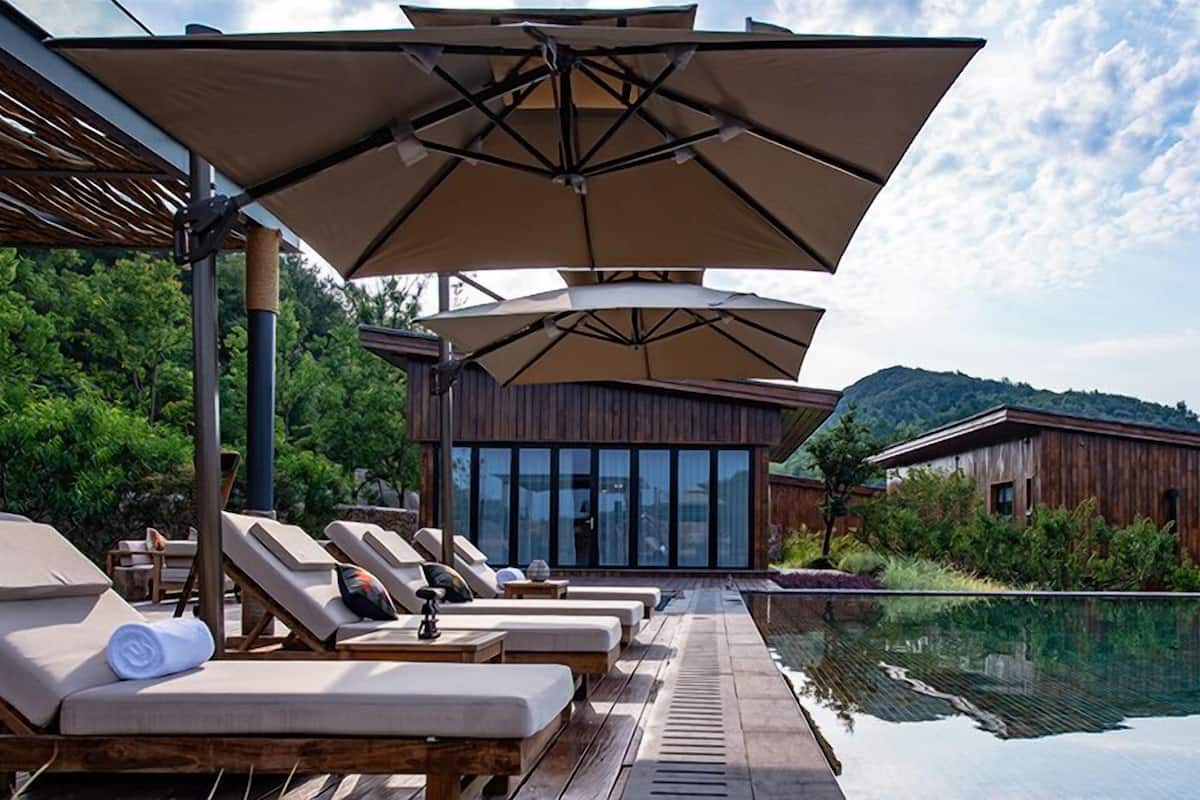 Un área junto a la piscina con sillas de descanso y sombrillas, un edificio de madera y una vista despejada del paisaje circundante.