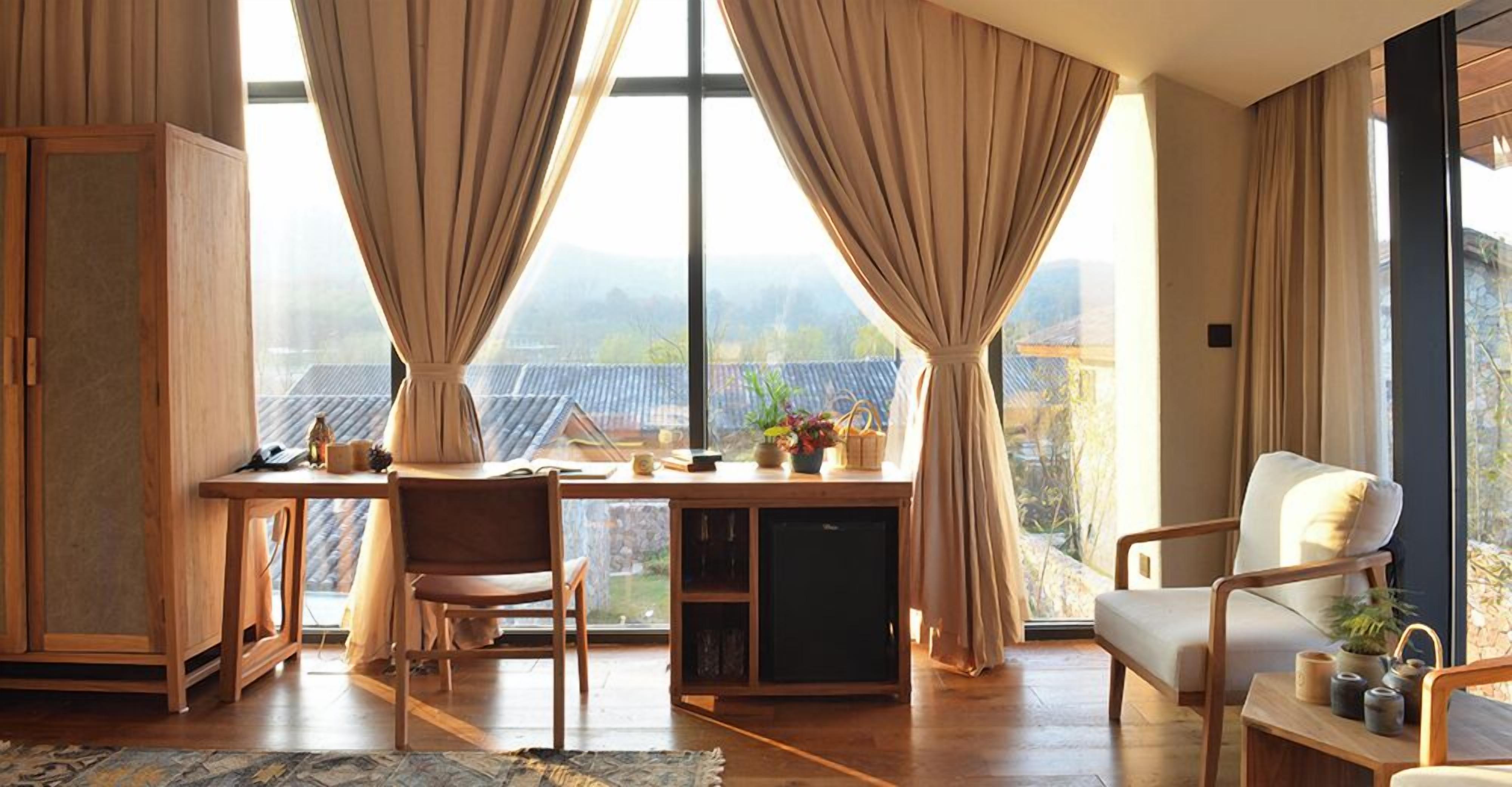 Ein Zimmer mit Schreibtisch, Stuhl und Blick auf eine gebirgige Landschaft durch große Fenster.