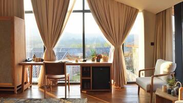 Ein Zimmer mit Schreibtisch, Stuhl und Blick auf eine gebirgige Landschaft durch große Fenster.