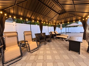 Une terrasse extérieure avec des carreaux hexagonaux, des meubles en osier et des guirlandes lumineuses.