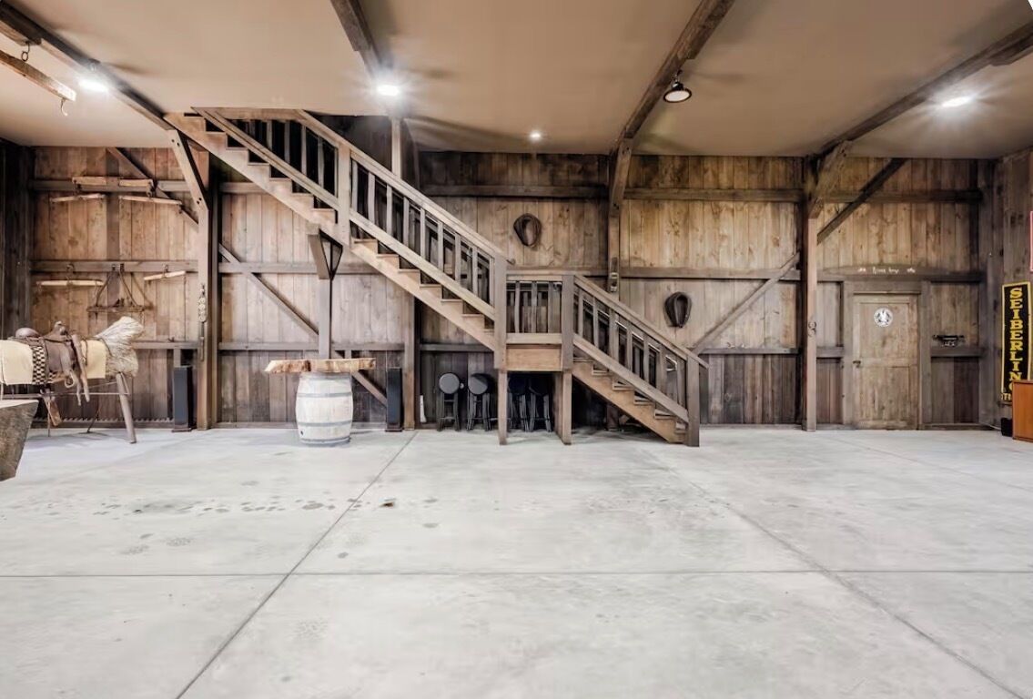 Un interior amplio con escalera de madera, suelo de concreto y decoración rústica.