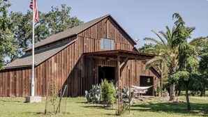 Une grange en bois avec un porche couvert, un mât pour drapeau et des cactus au premier plan.