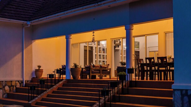 A building with a covered porch, steps leading to a door, and outdoor seating. - Martha's Barn (Mukono)