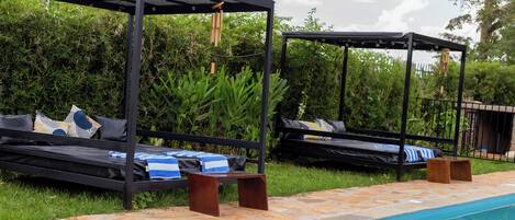 A poolside area with two black metal gazebos, lounge chairs, and a tiled pool.