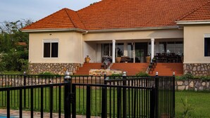 A house with a red-tiled roof, a stone foundation, and a black metal fence. - Martha's Barn (Mukono)