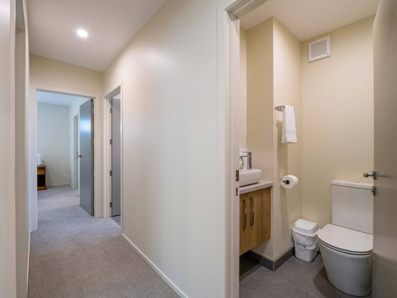 A narrow hallway leading to a bathroom with a toilet, sink, and cabinet.