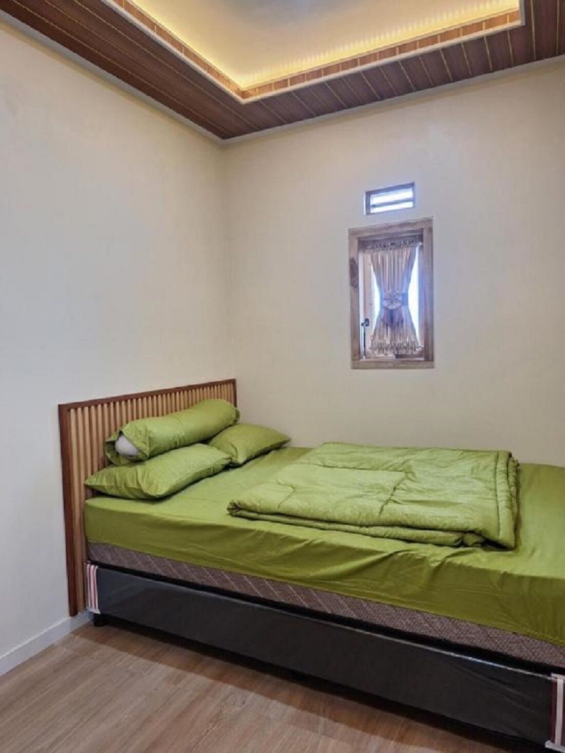 A bedroom with a wooden headboard, a green bedspread, and a small window with curtains.
