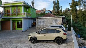 A beige SUV parked in front of a green building with a balcony. - Surya Bromo Homestay (Ngadisari)