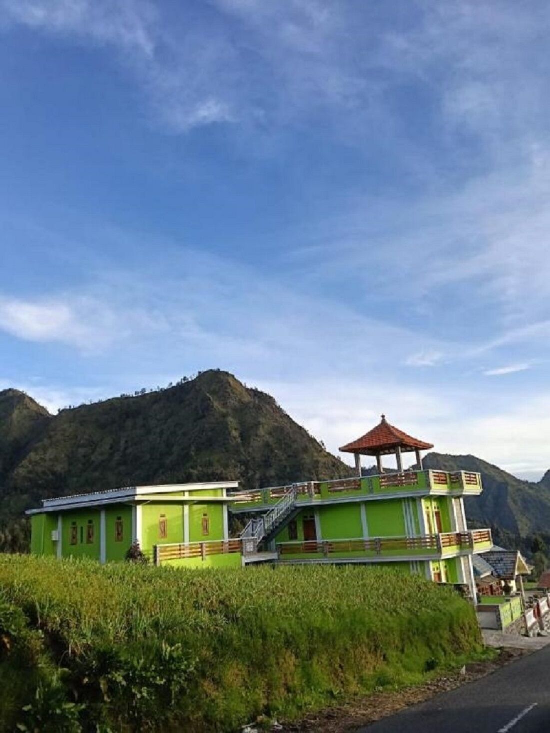 A green building with a red-roofed pavilion, surrounded by lush greenery and hills.